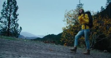 Kadın, sonbahar bulutlu bir akşamda sırt çantası ve sarı kazakla çakıllı dağ yolunda yürüyor. Yağmurlu bir günde turist gezintisi ve özgür hissetme. Seyahat tutkusu gezgini