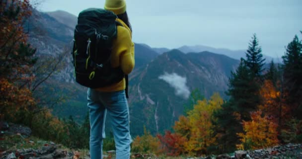ハイキングバックパック付きの黄色のセーターの女性は 秋の休暇旅行の夜に壮大な景色を望む山の端に立っています 女性旅行者は旅行で自由に楽しむ 手持ちのキーショット — ストック動画