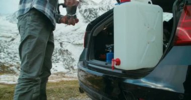 Tatil gezisindeki adamlar kampta bagajda kahve yapıyorlar. Erkek gezgin Moka pot kahve makinesine su dolduruyor. Seyahat macerasında.. 