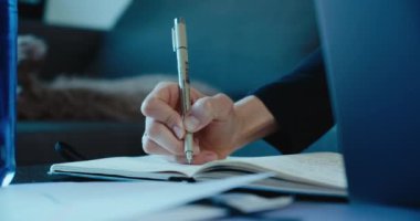 Ev kadınının kağıt defterine kalemle not tutarken yakın plan çekimleri. Freelancer ofiste çalışıyor ve yazıyor.