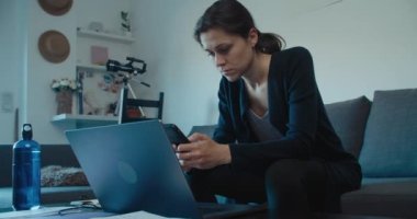 Kadın evde dizüstü bilgisayar ve cep telefonu kullanarak çalışıyor. Serbest çalışan kadın oturma odasında teknolojiyi kullanarak kanepede oturuyor.. 