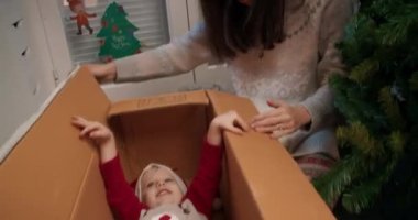 Noel ağacı kutusunda saklanan neşeli bir kız çocuğu. Neşeli aile kış tatiline hazırlanıyor evini süslüyor ve gülümsüyor.. 