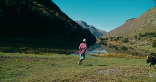 彼女の国内犬と美しい風景で山の湖畔を走っている陽気な女性 旅行でペットと遊ぶコンテンツ観光女性 — ストック動画