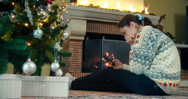 Žena Sedí Podlaze Hořícího Krbu Zdobené Vánoční Stromeček Pomocí Mobilního — Stock video