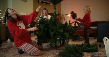 Neşeli insanlar oturma odasına yanan şömineyle Noel ağacı koyuyorlar. İki kadın ve çocuk kış tatili için oturma odasını dekore ediyorlar.. 
