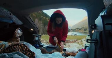 Dağ yolculuğunda kadın turist ekmek kesiyor güzel göl manzaralı kampta kahvaltı hazırlıyor.. 