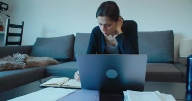 Freelancer woman work at home hand writing notes and using computer. Student preparing for exam in living room. 