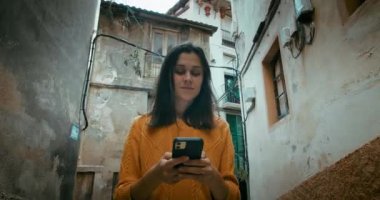 Eski şehir sokaklarında gezen çekici bir turist kadın ve yön bulma ya da arkadaşlarıyla iletişim kurmak için akıllı telefonu kullanıyor.