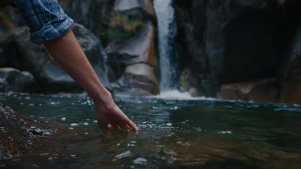 ゆっくりとした動きで滝のある山池の新鮮で清潔な水に触れる女性の手のクローズアップ — ストック動画