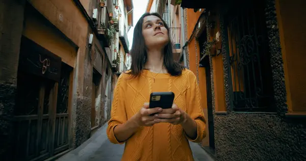 Çekici, neşeli bir kadın eski şehir caddesinde arkadaşlarıyla cep telefonu konuşarak ya da navigasyon için onu kullanarak yürüyor. 