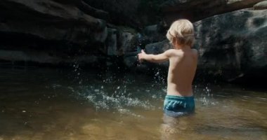 Çocuk yüzer ve şelaleli dağ göletinde suyla oynar. Yaz tatilindeki neşeli çocuklar Nehirde ferahlatıyorlar. 