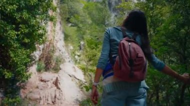 Sırt çantasıyla gezen kadın etrafı gözetliyor ve doğanın tadını çıkarıyor. Seyahat eden kadın turist dağ yolunda ormanda yürüyor.. 