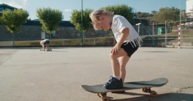 Şirin küçük kız kaykayın üzerinde durup babalardan kaykay öğrenmek için yardım istiyor. Çocuklar spor sahasında paten kaymaya çalışıyorlar.. 