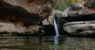 Akan şelale suyu ve uçurumdan dağ göletine düşmek. Göldeki su yüzeyinde dalgalar hareket ediyor. Rahatlamak için sakin bir manzara