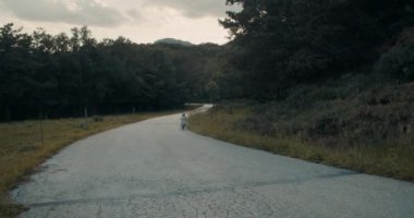 Yaz tatilinde dağ yolunda bisiklet sürerken çekilen yavaş çekim. Erkek ve kız kardeş gün batımında bisikletle