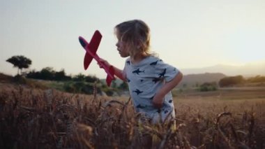 Şirin küçük kız yaz tatilinde kırsal alanda buğday tarlasında gün batımında yürüyor. Kırsal alanda oyuncak uçakla çayırdaki çocuk. 