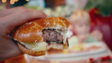 Yemek sırasında restoranda ısırılmış ve lezzetli bir burger tutan adam. Etli ve peynirli hamburgerin yakın çekimi. Fast food lokantası. 