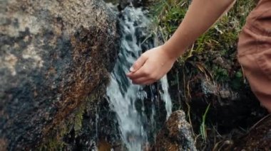 Çocuk dağ yolunda akan nehirde temiz su topluyor ve içiyor. Yürüyüş macerasına susadım. Çocuklar derede suya dokunur.. 