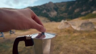 Turist dağ seyahati macerasında kampta açık bir moka kabı. İnsan elleri yakın çekimde doğada sıcak kahve yapıyor.
