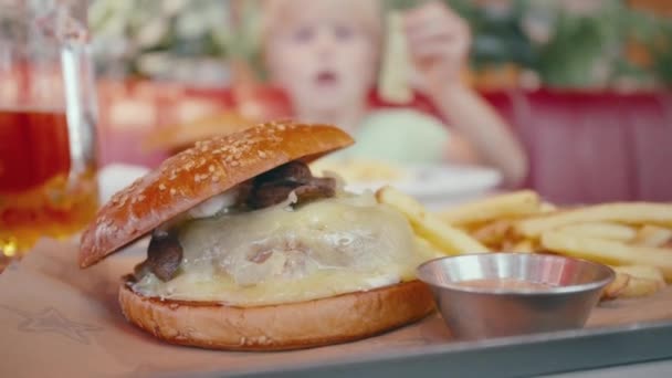 レストランでの美味しいハンバーガーは ぼやけた背景で子供を食べて撮影しました 不健康な食品コンセプト — ストック動画