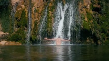 Memnun adam rahatlar ve dağ göletindeki şelale suyunun altında yüzer. İnsanlar tatilde doğanın tadını çıkarırlar.. 