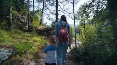 Çocuklu bir kadın yaz tatilinde yürür. Anne, kızı kucağına al ve dağlık yoldaki ağaçların arasında yürü.