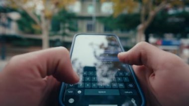 POV görüntüsü, bir adamın elinin yakın plan fotoğrafı. Şehir caddesinde akıllı bir telefonla mesajlaşması. Arka plandaki şehir ortamı..