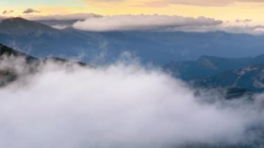 Gün batımında güzel bir dağ manzarası, bulutların üzerinde uçan bir dron. Destansı manzaranın sinematik hava görüntüsü