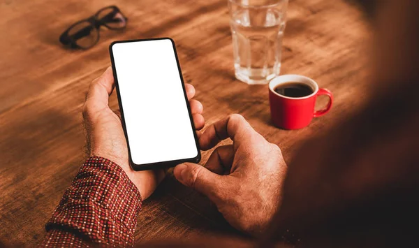 智能手机与空白 白色的 屏幕在男人的手中关闭 咖啡和棕色木制桌子为背景 免费复制 — 图库照片