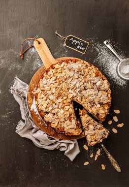 Homemade apple pie with flaked almonds crumble. Cake dessert captured from above (top view, flat lay) on a black chalkboard background. Free copy (text) space.