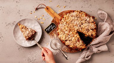 Homemade apple pie with flaked almonds crumble and a piece of cake on a plate. Dessert captured from above (top view, flat lay) on the grey background.
