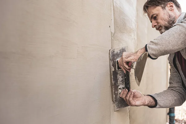 Renovation of the building facade - construction industry. Worker man (plasterer) plastering exterior walls of a house. Background with free copy (text) space.