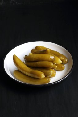 Cucumber pickle in a plate on a black background