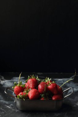 Siyah arka planda çilekler, metal kasede çilekler.