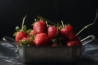Siyah arka planda çilekler, metal kasede çilekler.