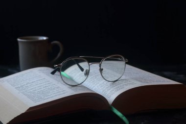 Siyah arka planda kalın bir kitap ve gözlük.