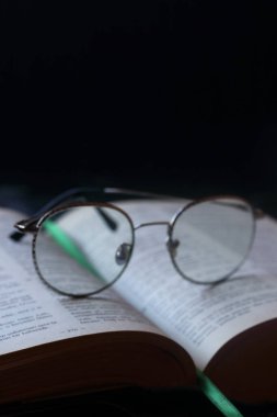 Siyah arka planda kalın bir kitap ve gözlük.