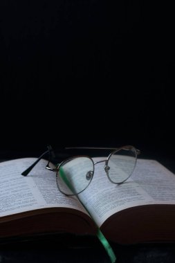 Siyah arka planda kalın bir kitap ve gözlük.