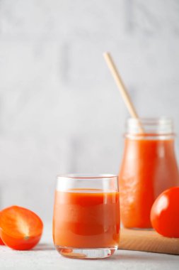 Beyaz tuğla bir duvarın arkasında, sebzeli bir bardak domates suyu.