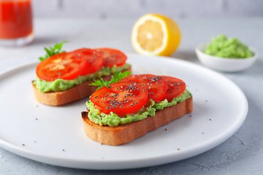 Beyaz tabakta avokado ve domatesli sağlıklı vejetaryen sandviç.