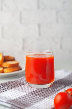 Beyaz tuğla bir duvarın arkasında, sebzeli bir bardak domates suyu.