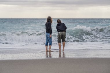 Anne ve kızı kıyı şeridinde yalınayak, ufukta bir şeye bakıyorlar, dikiz aynasından..