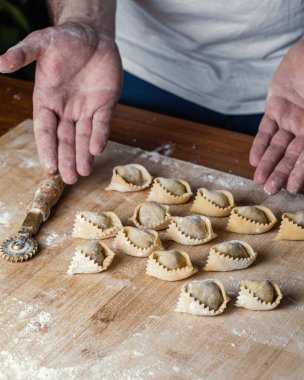 Şefin un un kaplı ellerine yakın çekim. Ravioli 'nin pişmeye hazır olduğunu gösteriyor. Ricotta ve ıspanak dolgulu Ravioli. Makarna bıçaklı ahşap çalışma masası. Dikey bileşim.