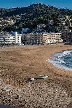 İspanya 'daki Costa Brava plajı, Tossa de Mar' daki sezon dışı Platja Gran manzarası. Issız sahilde kayıklar ve arka planda şehir manzarası. Kopya alanı ile dikey bileşim.