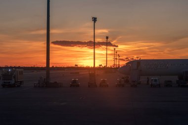 Barcelona-El Prat havaalanındaki pistin gün batımında gösterişli bir manzara. Ön planda, düşük maliyetli Wizz Air adlı ticari bir uçak, merdiveni ve servis araçları yerlerinde.. 