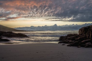 Güneş kumlu güzel bir plajın üzerinde batıyor, kayaların üzerine sıcak bir parıltı saçıyor ve dalgalar sahile çarptıkça dramatik ve huzurlu bir manzara yaratıyor. İspanya, Galiçya 'da Costa da Morte yakınlarında yer alan plaj.