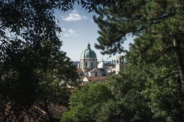 Duomo Nuovo manzarası yeşil ağaçlar tarafından çerçevelenmiş, görkemli kubbesi ve çan kulesi mavi gökyüzü ve kuzey İtalya 'daki Brescia, Lombardiya şehir manzarasına karşı duruyor..