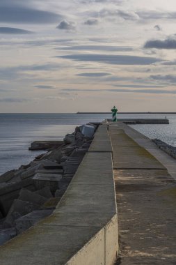 Korunmak için tetrapodların kullanıldığı uzun beton iskele, Barcelona 'da dramatik, bulutlu bir gökyüzünün altında yeşil ve beyaz bir deniz fenerine doğru ilerliyor..