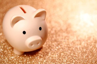 Parlayan Altın Arkaplan Kumbarası 'ndaki Piggy Bank, altın bir arka planda parlayan paralarla çevrili beyaz bir domuz kumbarasının yakın çekimi, birikimleri, zenginliği ve finansal güvenliği simgeliyor..