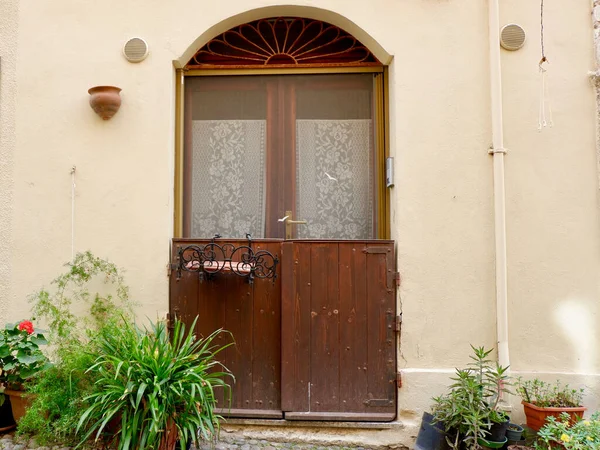 stock image Vintage rustic door made of wood with retro decorative elements on the beige worn building wall with house plants around in Alghero, Sardinia, Italy.